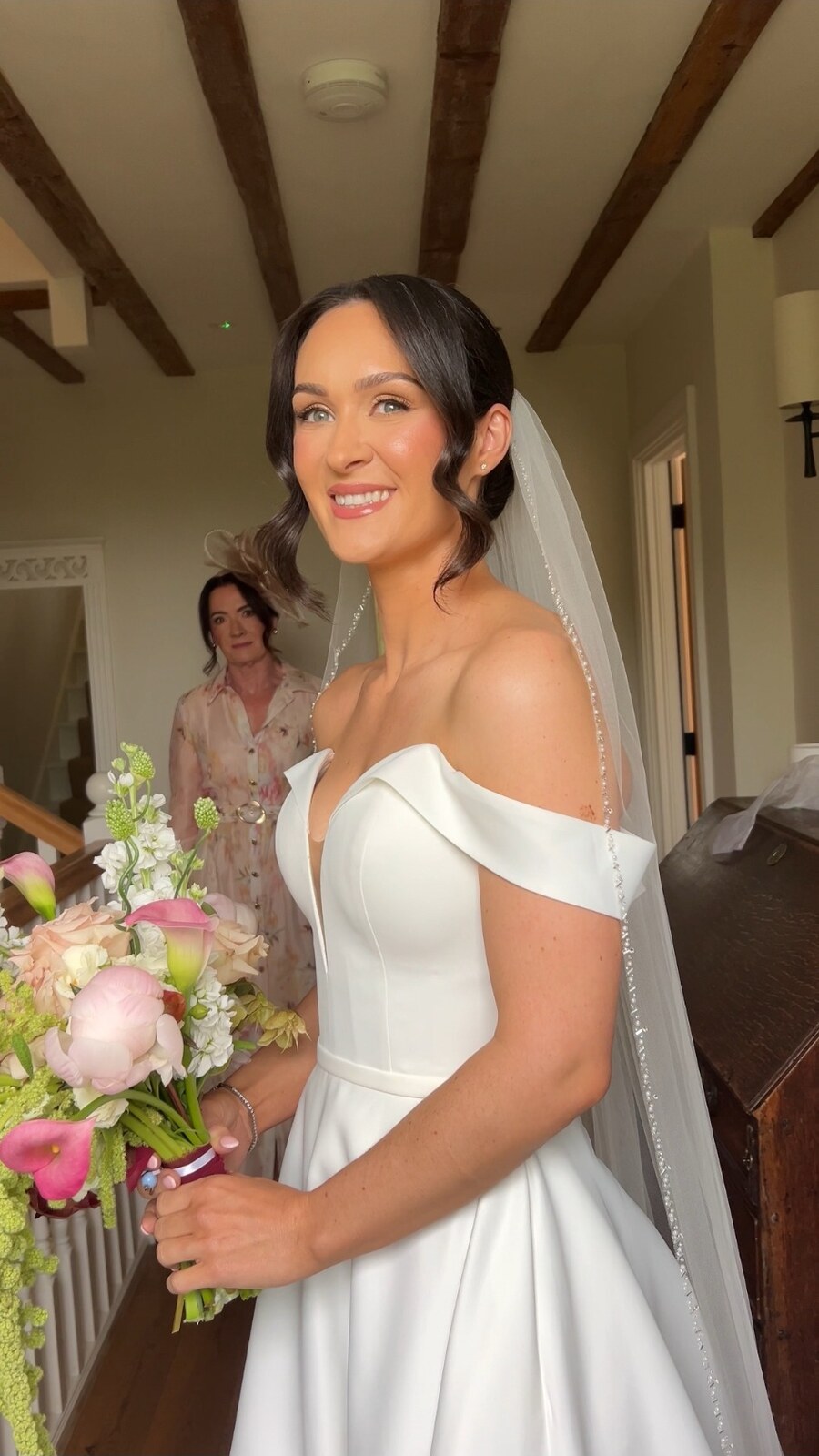 Dark-haired bride holding a pastel bouquet, with luminous skin, softly defined eyes and glossy nude lips, with makeup by Abby Christopher